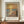 May include: Framed art print featuring an impressionist sunset seascape with golden sky reflecting on blue water, solitary figure walking on sandy beach, displayed on wooden sideboard with white ceramic vase and books in elegant room with cream walls and molding
