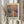 May include: Person holding framed impressionist painting print showing boats on water at sunrise with orange and blue reflections, Claude Monet signature visible below artwork, dried pampas grass in left hand, neutral beige clothing and curtained background