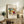 May include: Framed abstract art print displayed on rustic wooden sideboard in neutral-toned living room. Colorful Kandinsky-style artwork features bold brushstrokes in blues, yellows, reds, and greens with organic flowing forms. Light wood frame complements natural decor including fern plant, ceramic vase, stacked books, and cream upholstered furniture with brown leather cushion.