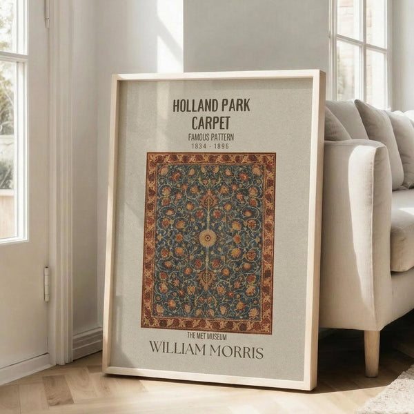 May include: Framed poster featuring an ornate vintage carpet design with intricate floral patterns in deep blues, oranges, and golds on cream background. Light wooden frame leans against white wall next to beige upholstered chair in bright, minimalist room with hardwood floors and large windows.