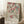 May include: A framed Japanese woodblock print featuring pink cherry blossoms on branches with three small birds - one flying at top, one perched mid-branch, and one at bottom. The artwork has muted earth tones with Japanese text in the upper right corner and "UTAGAWA HIROSHIGE" credit at bottom. The print leans against white paneled walls in a cozy corner setting with a coffee cup on a wooden block and cream blanket visible.
