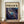 May include: Framed abstract art poster with swirling cosmic design in deep blues, purples, and teals with golden accents and circular forms, displayed on wooden sideboard next to white ceramic vase and stacked books in modern room with beige walls and white trim molding.