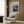 May include: Abstract expressionist artwork poster with swirling blue, purple and white paint strokes creating cosmic-like patterns, displayed in cream mat and frame on wood paneled wall above beige upholstered armchair with geometric patterned pillow, brass floor lamp and dark round side table with open book nearby