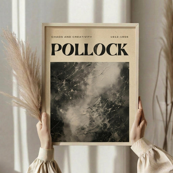 May include: Person in beige ruffle-sleeve top holding framed vintage-style Pollock poster with wheat stems. Abstract black and gray paint splatters and drips on cream background, titled "CHAOS AND CREATIVITY" with dates "1912-1956". Light wooden frame against soft neutral curtained window setting.