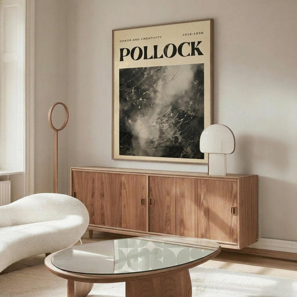 May include: A framed Jackson Pollock exhibition poster hanging above a mid-century modern wooden credenza in a minimalist living room. The vintage-style poster features "POLLOCK" in bold black letters with "CHAOS AND CREATIVITY 1912-1956" and displays an abstract black and white drip painting. The room has neutral beige walls, a white textured chair, glass-top coffee table, and modern lighting fixtures creating warm shadows on the polished floor.