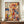 May include: Abstract expressionist artwork with energetic paint splatters, drips and gestural brushstrokes in vibrant red, blue, yellow and black against cream background. Framed in thin brown frame, displayed on wooden sideboard next to white ceramic vase and stacked books in elegant room with white paneled walls.