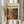 May include: Person in cream ruffle-sleeve top holding framed abstract art poster featuring dynamic orange and dark green paint splatters and drips. Dried pampas grass visible on left side. Light wooden frame against neutral background with soft natural lighting.