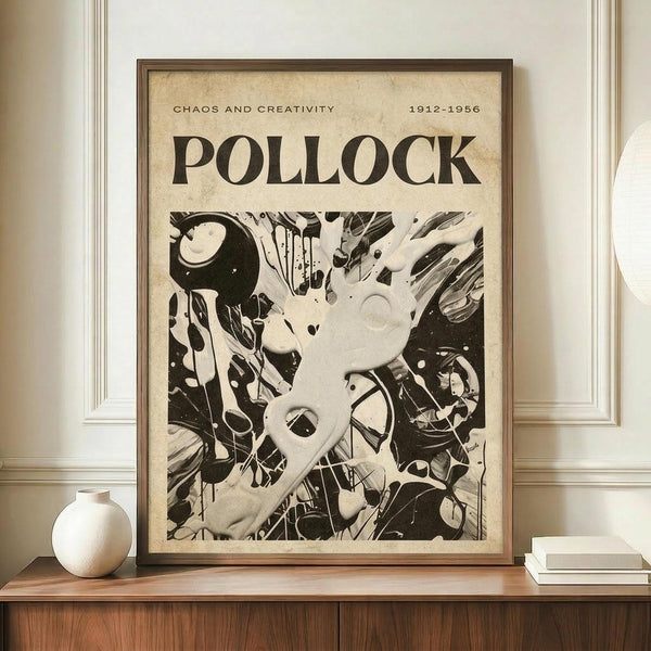May include: Framed vintage-style poster with "POLLOCK" and "CHAOS AND CREATIVITY 1912-1956" text above abstract black and white paint splatter artwork. Brown wooden frame displayed on light wood sideboard next to white ceramic vase and books against cream walls with white wainscoting.