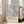 May include: Framed abstract art poster with pale blue and gray brushstrokes leaning against white wall next to beige sofa. The artwork features organic splatters and linear marks in muted tones. Exhibition-style text appears below the abstract image on cream background within light wood frame on hardwood floor.