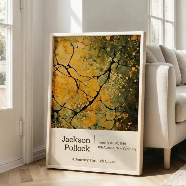 May include: Framed poster print featuring abstract artwork with flowing yellow and green organic shapes, circular bubbles, and dark branching lines resembling tree branches or neural networks. The piece has an earthy, natural color palette transitioning from golden yellow to deep green. Below the artwork is white text reading "Jackson Pollock" with exhibition details and "A Journey Through Chaos." The poster leans against a white wall next to a beige upholstered sofa in a bright, minima