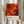 May include: Person in beige ruffled sleeves holding framed abstract art poster featuring vibrant red, orange, and yellow swirling paint with black accents and circular elements. White matted frame against neutral curtained background with dried pampas grass visible on left side.