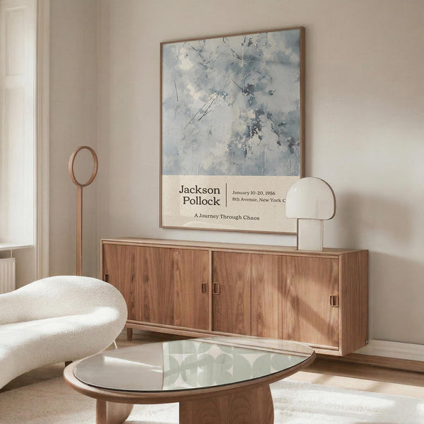 a modern living room with a large abstract painting hanging on the wall above a wooden cabinet. The room has a white sofa, a glass coffee table, and a lamp on a side table.