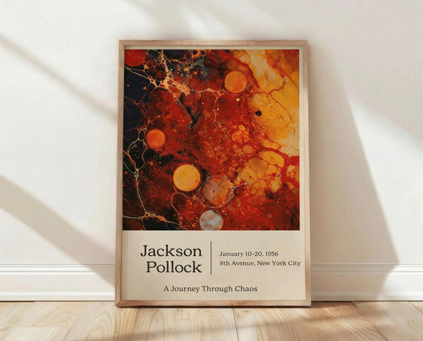 May include: Framed abstract art poster with vibrant red, orange, and yellow bubble-like patterns resembling fluid or cellular structures against dark background. Text reads "Jackson Pollock" with exhibition details and "A Journey Through Chaos." Light wood frame leans against white textured wall on blonde hardwood floor with soft natural lighting creating diagonal shadows.
