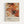 Abstract expressionist artwork featuring energetic splashes and drips of orange, red, black and white paint with thin white lines creating a web-like pattern across the composition. Below the artwork is text reading "Jackson Pollock" with exhibition details "January 10-20, 1956 8th Avenue, New York City" and "A Journey Through Chaos." The poster is displayed in a light wooden frame against a white wall.