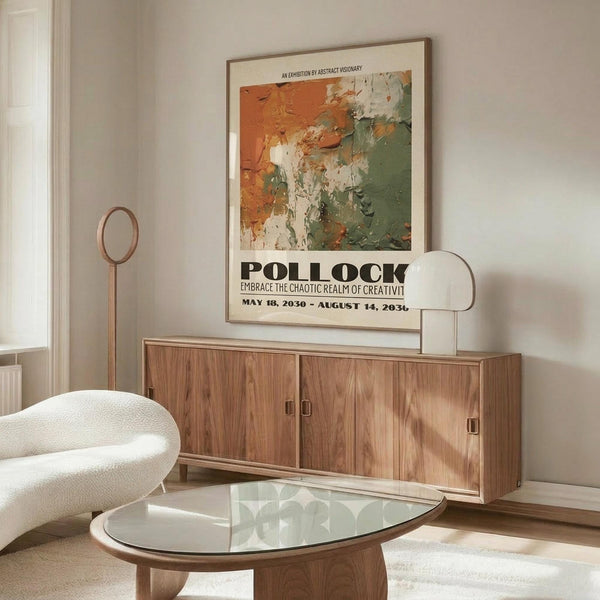 May include: Abstract art poster with orange, green and white paint splatters hung above wooden credenza in modern living room. White upholstered chair and glass oval coffee table visible. Poster shows textured brushstrokes in earth tones with bold black text below the artwork. Natural lighting creates soft shadows on cream walls.