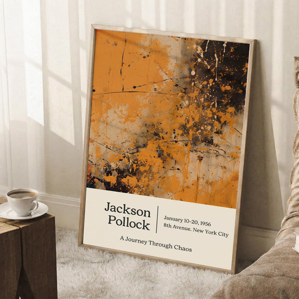 May include: Framed abstract art poster with orange and black paint splatters in Jackson Pollock's drip painting style, leaning against white wall next to beige armchair. White coffee cup on wooden side table. Cream-colored frame with white text panel showing exhibition details. Soft natural lighting creates window shadows on wall. White textured rug underneath.