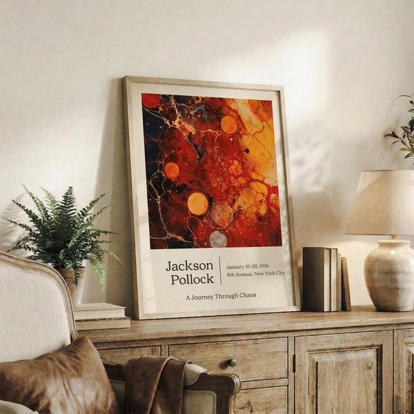 May include: Framed abstract art poster with vibrant red, orange, and black splattered paint design in warm wood frame, displayed on rustic wooden sideboard alongside fern plant, ceramic vase, and leather armchair in cozy neutral-toned living room setting with natural lighting