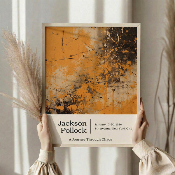 May include: Person in cream sweater holding framed abstract art poster with orange and black paint splatters in Pollock's signature drip style. White frame against soft neutral background with dried pampas grass. Exhibition-style layout with artist name, dates, and "A Journey Through Chaos" text below artwork.