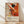 May include: Framed abstract art poster featuring Jackson Pollock's signature paint splatter style with vibrant orange, black, and cream colors. Dynamic brushstrokes and paint splatters create energetic movement across the canvas. Exhibition details showing January 10-20, 1956 at 8th Avenue, New York City with subtitle "A Journey Through Chaos." Natural wood frame displayed against white wall on light wooden floor with soft shadows.