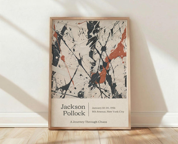 May include: Framed abstract art print with chaotic black paint splatters and orange-red accents on cream background, displayed against white wall on light wood floor. Poster features Jackson Pollock text and exhibition details below artwork. Natural lighting creates soft shadows across the scene. Light wood frame complements the warm wooden flooring.
