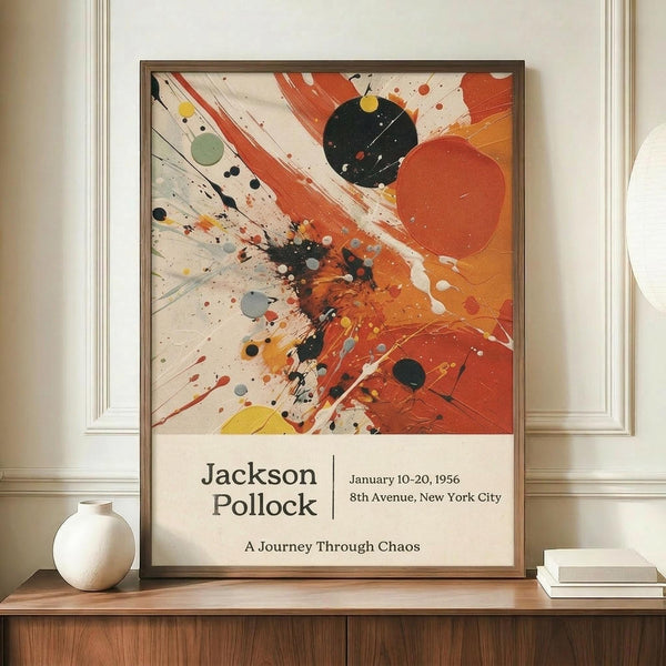 May include: Framed Jackson Pollock exhibition poster featuring abstract expressionist artwork with dynamic orange, red, black and yellow paint splatters and brushstrokes on cream background. Exhibition details read January 10-20, 1956, 8th Avenue, New York City, "A Journey Through Chaos." Displayed on wooden sideboard beside white ceramic vase and stacked books against cream wainscoted wall.