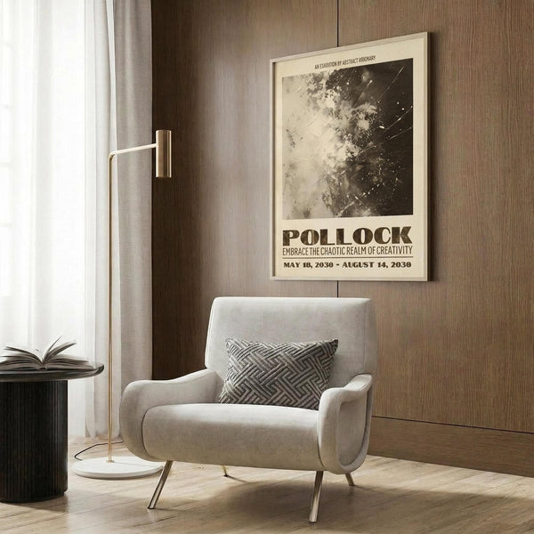 May include: A beige poster featuring Jackson Pollock's abstract black and white splatter artwork with exhibition text below, displayed in light wooden frame on wood-paneled wall. Modern living room setting shows cream upholstered chair with geometric patterned pillow, brass floor lamp with white shade, and dark round side table with open book.