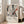 May include: Abstract expressionist artwork poster with black paint splatters, drips and orange-red accents on cream background, displayed in light wood frame leaning against white wall next to beige upholstered chair in bright, naturally-lit room with large windows and hardwood floors.