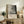 May include: Abstract black and gray splattered artwork in light wood frame, displayed on rustic wooden sideboard with fern plant, ceramic vase, and books. Neutral living room setting with beige chair and soft natural lighting. Exhibition-style poster features textured paint splatters and drips in monochromatic tones.