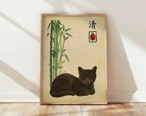 May include: Framed artwork displaying a sleeping brown tabby cat beside green bamboo stalks on cream background with Japanese characters and red stamp seal, shown in light wood frame leaning against white wall on wooden floor with soft natural lighting