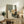 May include: Abstract geometric artwork with sage green, beige, and gray rectangular shapes plus orange circle, combined with silhouette of pine tree branches, displayed in light wood frame on rustic wooden sideboard alongside fern plant, books, and ceramic vase in neutral-toned living room