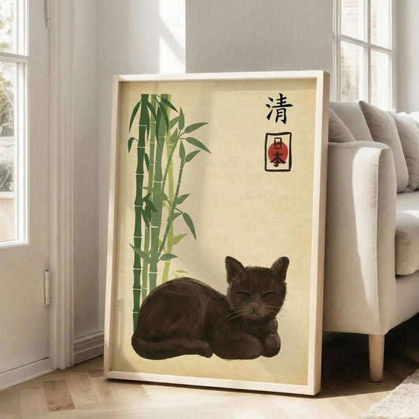 May include: Framed poster with cream background featuring a sleeping brown tabby cat, green bamboo stalks, and black Japanese characters with red accent. Light wood frame leaning against white wall next to beige upholstered chair in bright, airy room with large windows and hardwood floors.