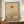 May include: Minimalist Japanese-inspired artwork in wooden frame on walnut credenza, featuring geometric orange sun, curved beige forms, and silhouetted tree against cream background with vertical line element. White ceramic vase and stacked books beside framed print in elegant room with white paneled walls.