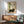May include: Framed poster featuring a dark brown cat resting beside green bamboo stalks on cream background with Japanese characters and red stamp. Shown hanging above wooden credenza with white ceramic lamp in modern living room with mint green upholstered chair and round wooden coffee table. Natural sunlight creates geometric shadows on white wall.