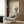 May include: Framed poster print featuring cute cartoon black cat with large yellow eyes sitting beside green bamboo stalks, with Japanese characters above. Modern living room setting with beige armchair, geometric patterned pillow, gold floor lamp, and wood-paneled wall. Warm neutral tones throughout scene.