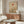 May include: Minimalist Japanese-inspired artwork hanging above a wooden credenza in a modern living room. The poster features a beige background with a red sun, curved line, small tree silhouette, and geometric shapes in earth tones. White mushroom table lamp and wooden floor lamp flank the credenza. White curved chair and glass-top coffee table complete the serene, mid-century modern space with warm wood tones.