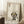 May include: Framed poster print featuring a cute black cat with large yellow eyes sitting next to green bamboo stalks, with Japanese characters at the top, displayed in a light wood frame leaning against a white wall corner. A white coffee cup sits on a wooden side table nearby, with a textured white rug and beige blanket visible in the cozy room setting.