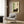 May include: Framed Japanese-style artwork featuring a dark gray tabby cat resting beside green bamboo stalks on cream background with red seal stamp and black characters, displayed on wood paneled wall above beige upholstered armchair with geometric patterned pillow, brass floor lamp and side table visible in modern living room setting