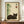 May include: Framed Japanese-style artwork featuring a sleeping dark gray cat beside green bamboo stalks on cream background, displayed on wooden sideboard with white ceramic vase and books, against white paneled wall in modern interior setting.