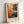 May include: Framed abstract expressionist art print in light wood frame leaning against white wall. Artwork features vibrant paint splatters and drips in orange, red, blue, black and white with dynamic brushstrokes radiating from center. Text below reads "POLLOCK Expressive Expressionist Movement" in black letters on cream background.
