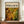 May include: Framed abstract art poster with swirling green and golden yellow paint splatters in Jackson Pollock's signature drip painting style, displayed on wooden sideboard next to white ceramic vase and stacked books. The poster shows "CHAOS AND CREATIVITY" and "POLLOCK" text at top with "1912-1956" dates. Warm beige walls with white wainscoting visible in background. The organic, flowing paint creates circular and linear patterns across the canvas reproduction.