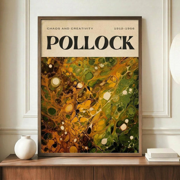 May include: Framed abstract art poster with swirling green and golden yellow paint splatters in Jackson Pollock's signature drip painting style, displayed on wooden sideboard next to white ceramic vase and stacked books. The poster shows "CHAOS AND CREATIVITY" and "POLLOCK" text at top with "1912-1956" dates. Warm beige walls with white wainscoting visible in background. The organic, flowing paint creates circular and linear patterns across the canvas reproduction.