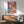 May include: Vibrant abstract artwork with colorful paint splatters and drips in pink, blue, yellow, and red tones, displayed in thin wooden frame above modern walnut credenza. Mid-century modern living room setting with sage green upholstered chair, round wooden side table, white ceramic table lamp, and natural sunlight streaming across white wall.