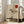 May include: Framed minimalist poster featuring a lone tree silhouette against a beige textured background with geometric black lines and a red circle sun. The artwork is displayed in a light wood frame, leaning against a white wall next to a beige upholstered sofa in a bright living room with large windows and natural lighting.