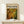 May include: Framed abstract expressionist art poster displayed on light wood console table against white wall. Features dynamic swirling composition in warm oranges, yellows, and forest greens with scattered circular forms and flowing paint-like textures. Small white gift box with green sprig sits nearby. Natural wood frame complements minimalist modern interior setting.