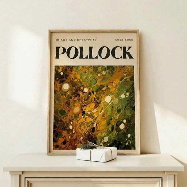 May include: Framed abstract expressionist art poster displayed on light wood console table against white wall. Features dynamic swirling composition in warm oranges, yellows, and forest greens with scattered circular forms and flowing paint-like textures. Small white gift box with green sprig sits nearby. Natural wood frame complements minimalist modern interior setting.