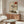 May include: Modern living room setting with cream walls featuring an abstract artwork displaying a delicate black tree silhouette against beige background with red circle sun and geometric black lines. Below sits a mid-century walnut credenza with white mushroom table lamp, white curved lounge chair, and oval glass coffee table on wooden base.