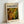 May include: Framed poster print featuring Jackson Pollock's abstract expressionist artwork with swirling patterns of green, yellow, orange and white paint in his signature drip style. The print has "POLLOCK" in bold black letters at top with "CHAOS AND CREATIVITY 1912-1956" subtitle. Natural wood frame leaning against white wall corner on light surface, showing warm lighting and shadows.