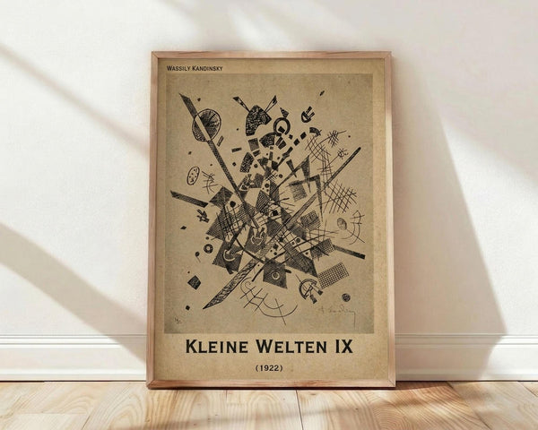 May include: Framed abstract art print in light wood frame leaning against white wall on wooden floor. Beige poster features black geometric shapes, lines, and patterns in dynamic composition. Soft natural lighting creates diagonal shadows across white fabric backdrop.