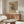 May include: Abstract geometric art print by Wassily Kandinsky displayed above wooden sideboard in minimalist living room. Black angular shapes, lines and patterns on beige background in gold frame. Modern white curved chair, glass oval coffee table, and warm wood furniture create contemporary Scandinavian-style interior with neutral tones.