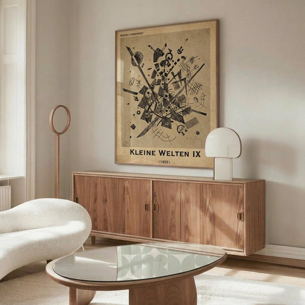 May include: Abstract geometric art print by Wassily Kandinsky displayed above wooden sideboard in minimalist living room. Black angular shapes, lines and patterns on beige background in gold frame. Modern white curved chair, glass oval coffee table, and warm wood furniture create contemporary Scandinavian-style interior with neutral tones.